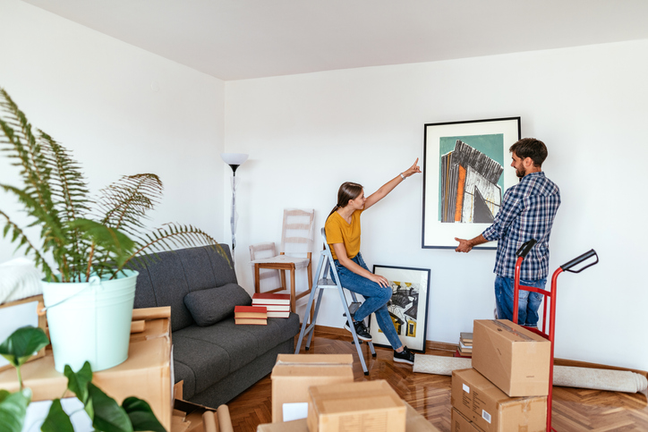Couple moving in new apartment, woman and man putting picture on the wall